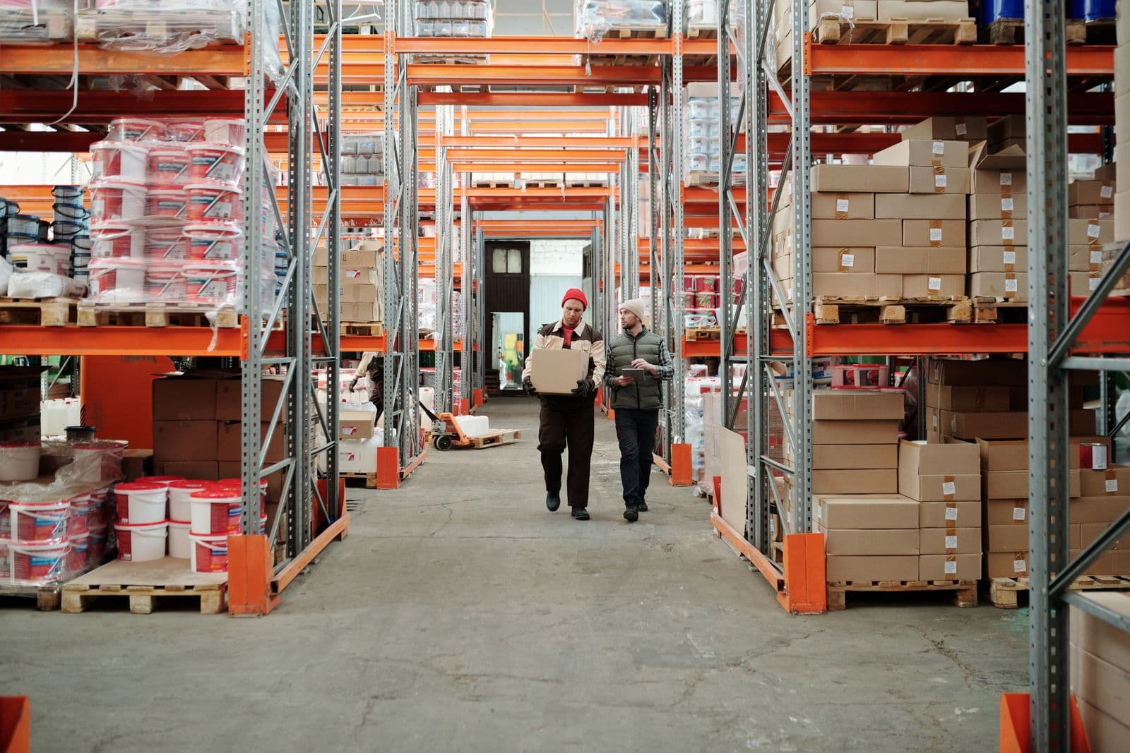 Two warehouse workers handling a package among stocked shelves