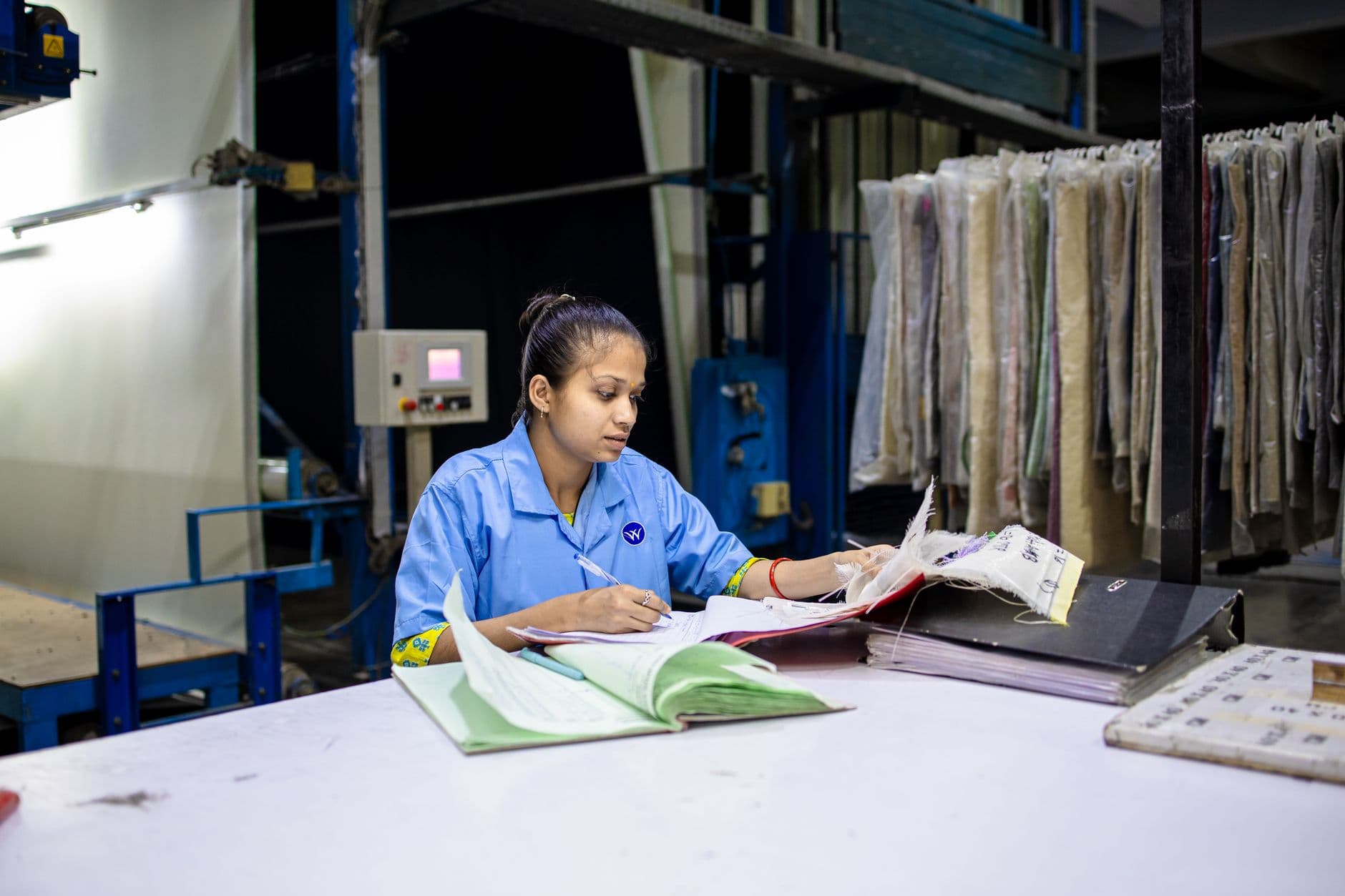 A small manufacturer stands on the shop floor reviewing shipping and payroll paperwork.